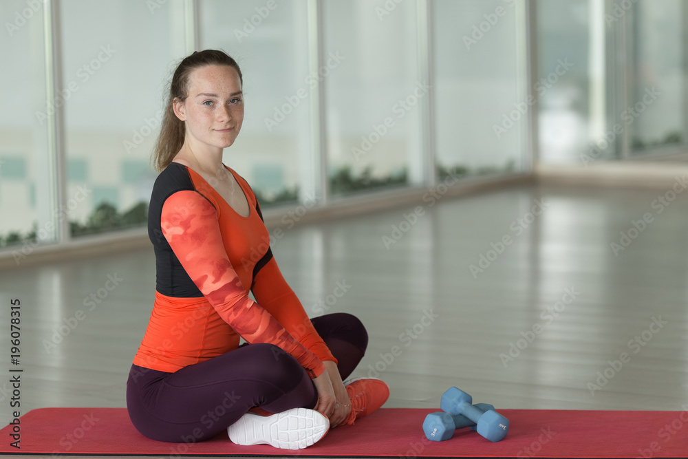 young girl in suit sitting on rug next to dumbbell in an empty gym during workout young girl in suit sitting on rug next to dumbbell in an empty gym during workout