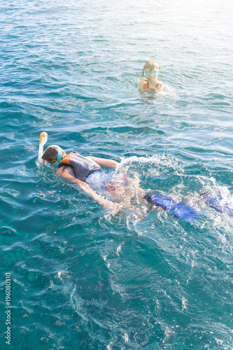 Two teenagers enjoying snorkeling in turquiose tropical sea. Girl swimming on sea surface and boy swimming and looking at camera.