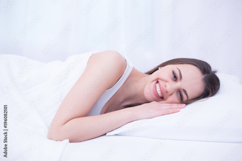 Young beautiful smiling woman lying in white bed at home waking up from sleep. Young beautiful smiling woman lying in white bed at home waking up from sleep.