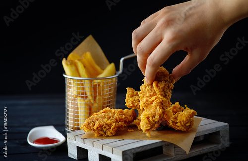 Female hand touching fried chicken breasts. Junk food concept. Black background