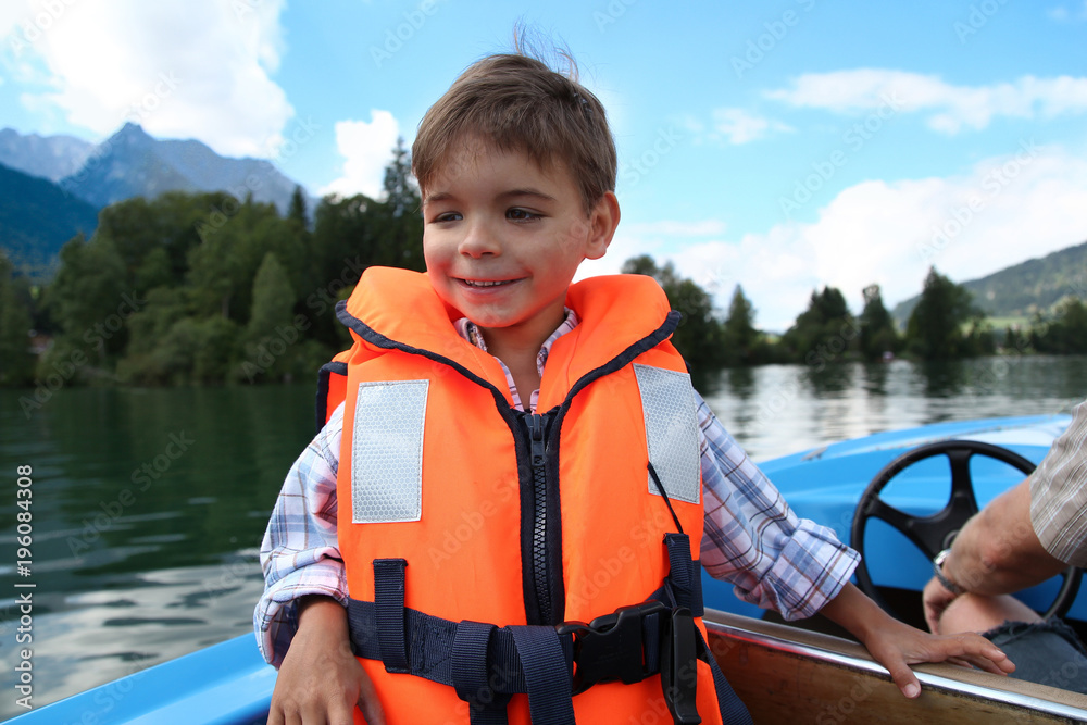 Junge in oranger Schwimmweste an Bord eines Motorbotes Junge in oranger Schwimmweste an Bord eines Motorbotes