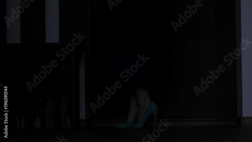 Legs of alcoholic drunken woman in mini skirt and high heels entering door with wine bottle in hand. Intoxicated female holding alcohol bottle throwing coat to the floor and walking to bed stumbling