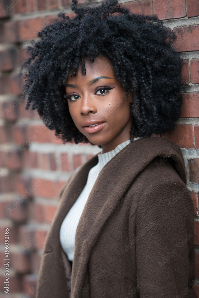 Beautiful African American with black, curly hair leaning against brick  wall Stock Photo | Adobe Stock
