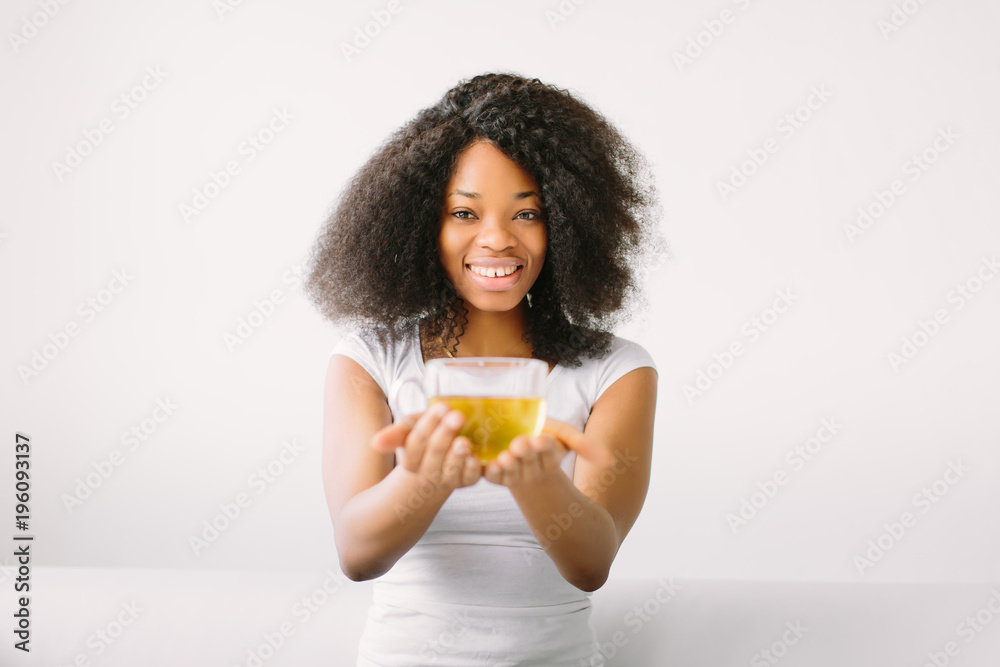 An African American young woman sitting in the lotus position on white bed with cup of tea An African American young woman sitting in the lotus position on white bed with cup of tea