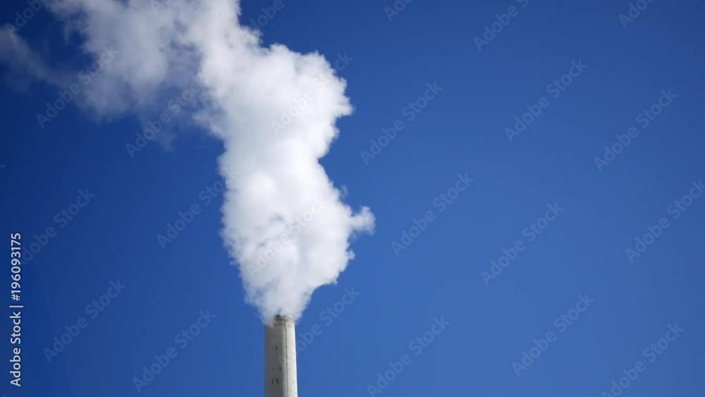 A Smoke stack blowing smog or water vapor our of tower on clear sky backdrop - Close Up