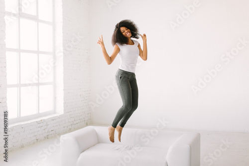 An African American young woman jumping on white bed