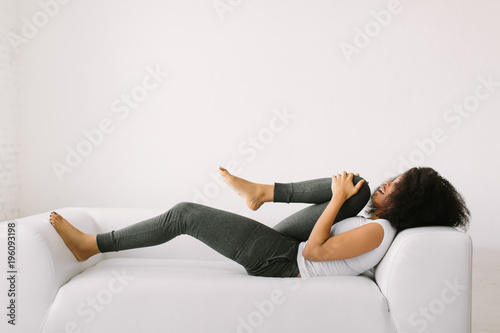 An African American young woman lying on a white bed and doing physical exercises