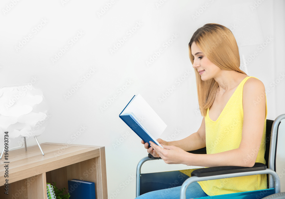 Young woman in wheelchair reading book indoors Young woman in wheelchair reading book indoors