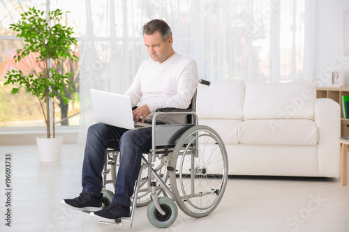 Mature man in wheelchair using laptop indoors