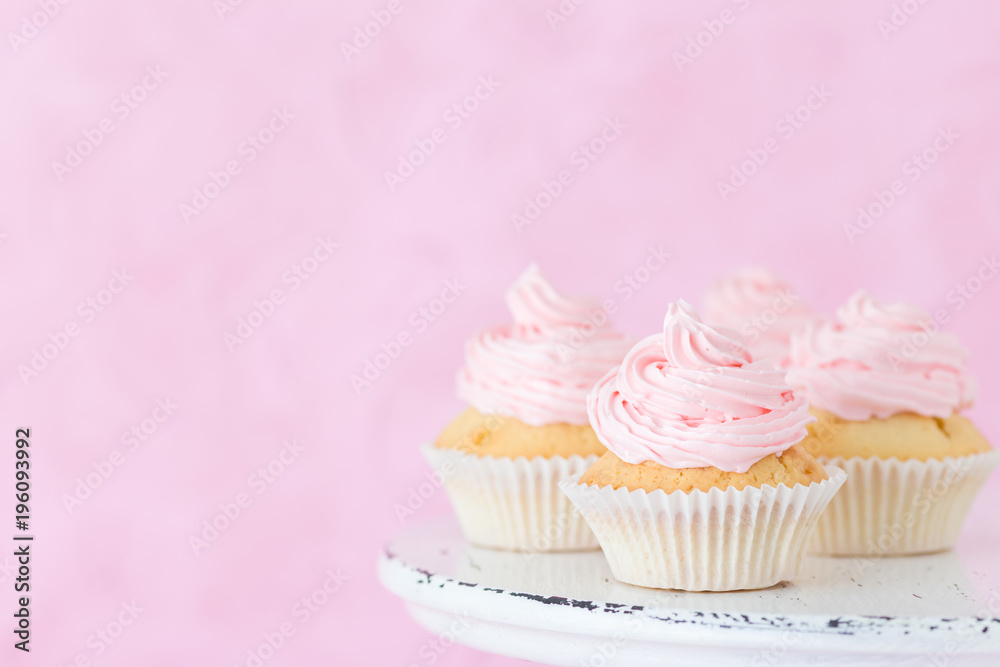 Cupcake decorated with pink buttercream on shabby shic stand on pastel pink background.