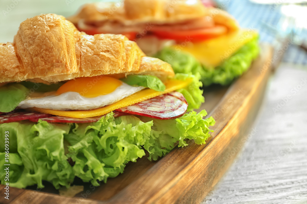 Obraz premium Wooden board with tasty croissant sandwich on table