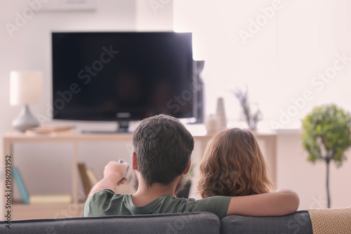 Happy couple watching TV while sitting on sofa at home