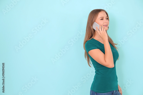 Young woman talking by mobile phone on color background