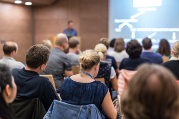 Business and entrepreneurship symposium. Speaker giving a talk at health care workshop meeting. Audience in conference hall. Rear view of unrecognized participant in audience.