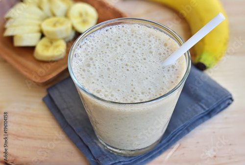 Smoothie with banana in the glass, fresh bananas on the wooden background