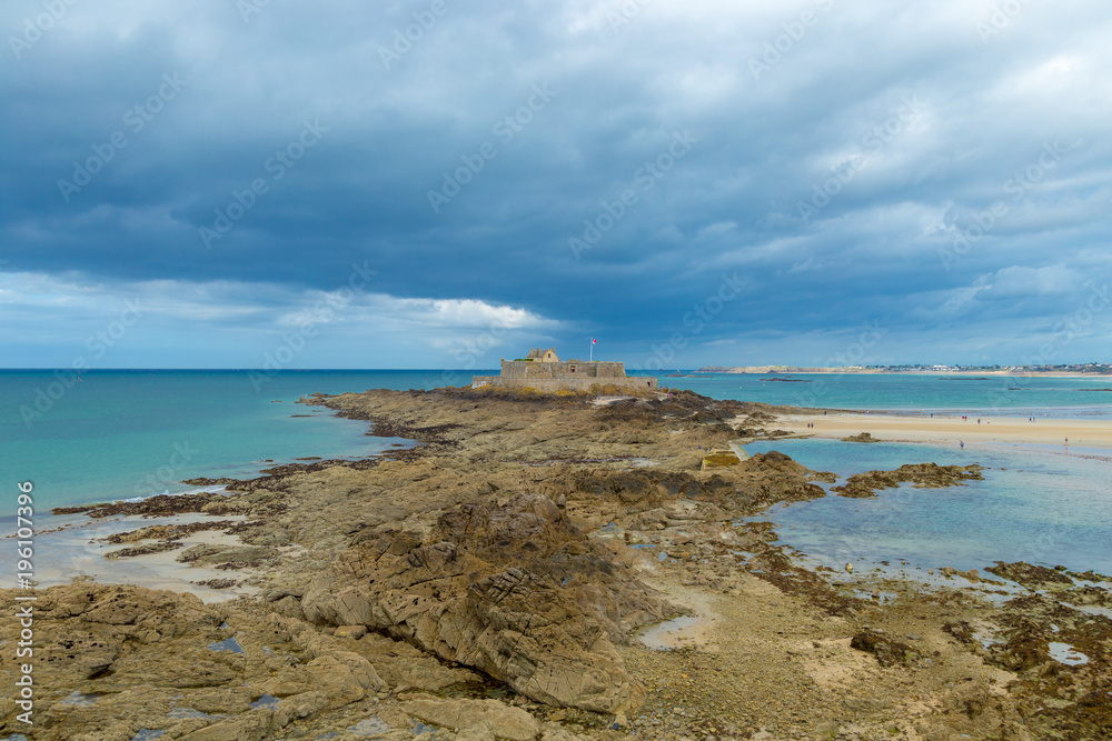 Saint Malo beach, with Fort National and rocks during low tide and grey stormy sky. Brittany, Europe
