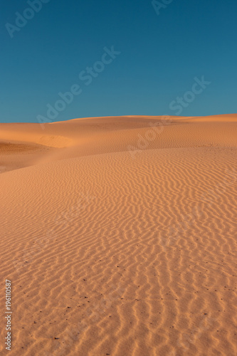 Empty sand dune view with clear blue sky.