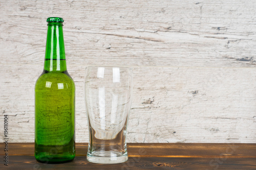green beer bottle with empty glass on pub table