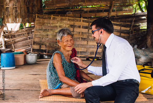 Male Doctor listening heart beat and breathing of Elderly Woman with Stethoscope with First Aid Medical Box.Community Health and Development Hospital In Remote Areas Development Fund Concept. photo