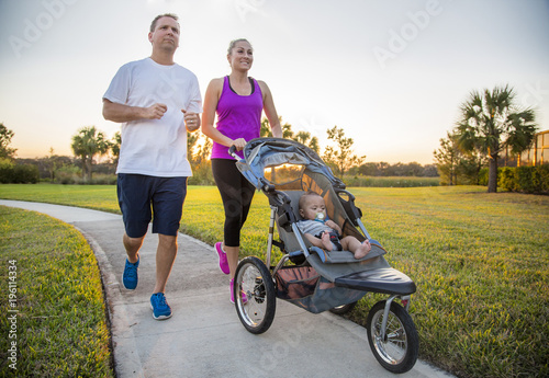 Couple exercising and jogging together at the park pushing their baby in a stroller