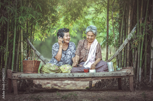 Two Asian old women sat happily on the bed in a Thai bed. Communication concept with descendants over the phone.