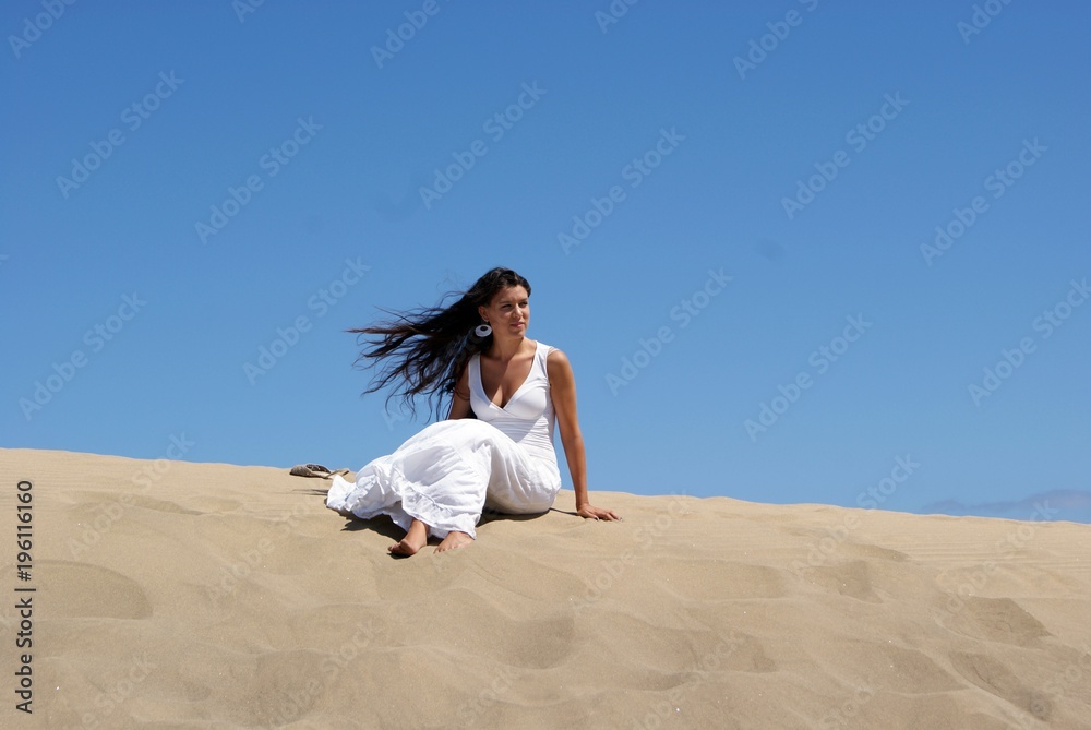 Beautiful brunette young woman bride sitting in sand dunes with the sky background