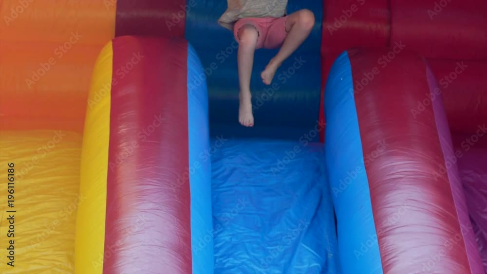Slow motion a girl slides down a huge inflatable slide during a party