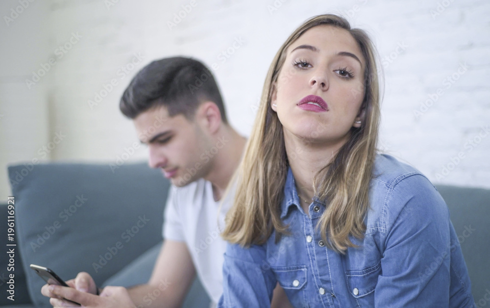 young attractive couple in relationship problem with internet mobile phone addiction boyfriend ignoring sad neglected and worried girlfriend at home