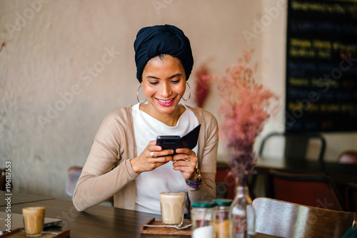 Photography Portrait of a young Muslim Malay woman sitting in a cafe and using her smartphone as she enjoys her morning coffee
