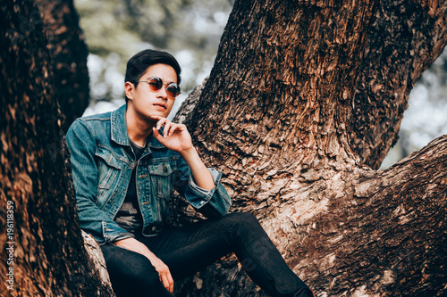 Portrait asian young men wearing sunglasses and jeans shirts sitting on tree