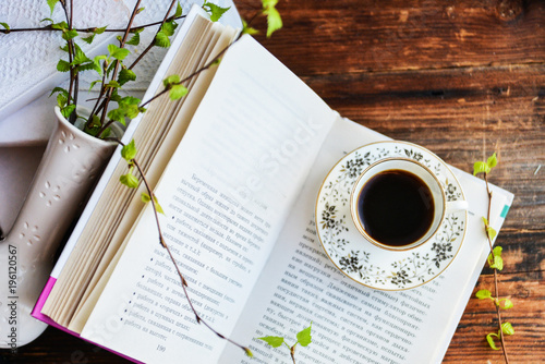 open book, coffee mug, branches with green leaves, the concept of love for reading, spring and freshness