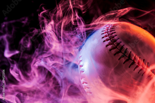 Canvas Print Close up of a white baseball ball in multi-colored red smoke from a vape on a bl