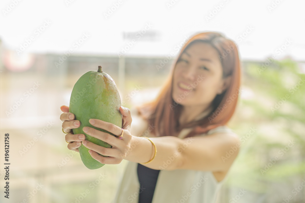 Fototapeta premium woman holding a fresh Mango in her hand and blur of woman
