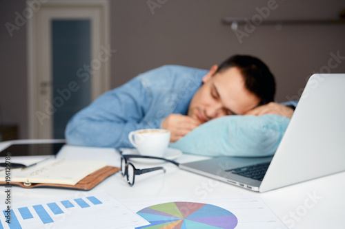 Blurry images. Stressful male sleeping on the table with laptop and documents. Sleepworking after long junkets of effort.