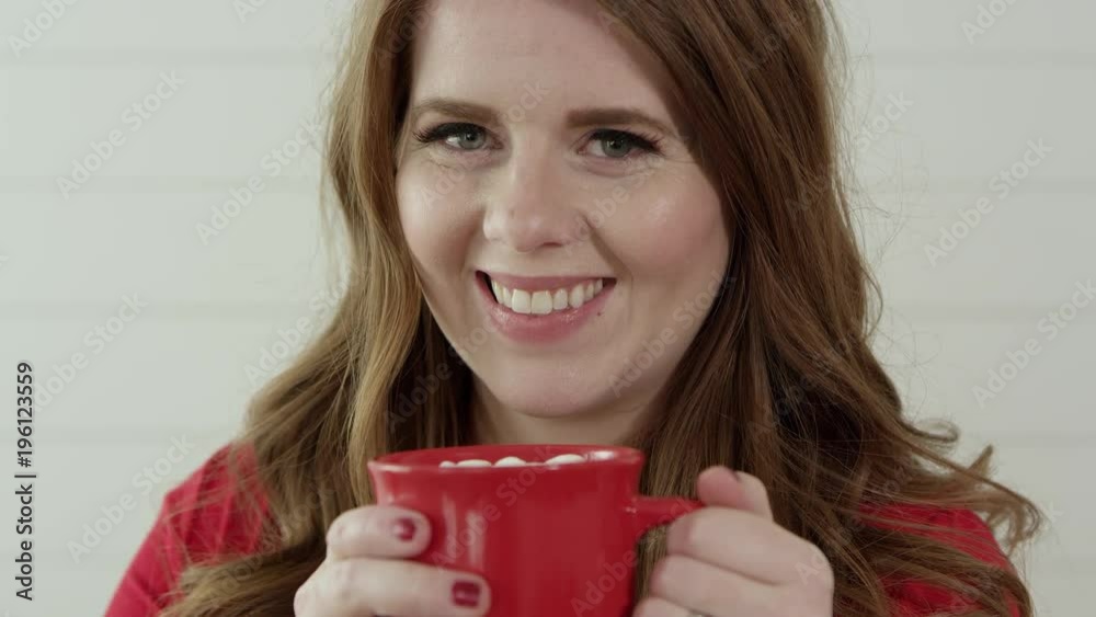 Woman smiling as she raises mug of hot chocolate with marshmallow to her face.