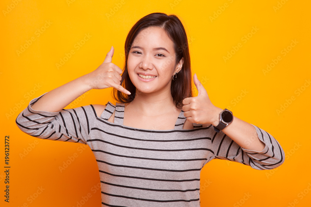 Young Asian woman thumbs up show with phone gesture. Young Asian woman thumbs up show with phone gesture.