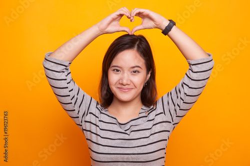 Young Asian woman gesturing heart hand sign.