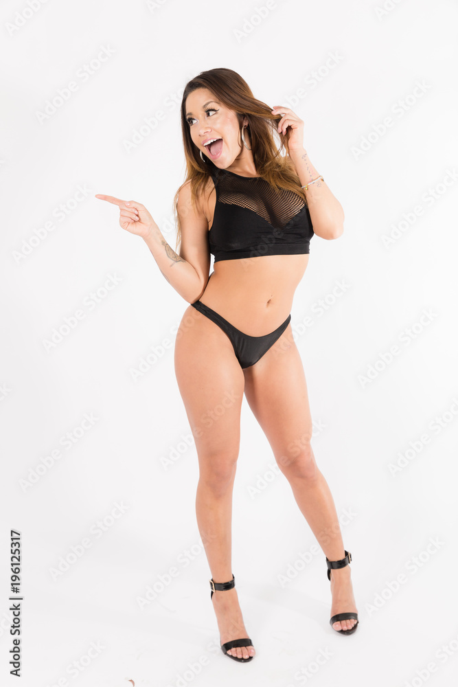 Young fit hispanic woman in black two piece and black high heels posing on a white background Young fit hispanic woman in black two piece and black high heels posing on a white background