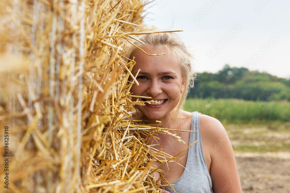 A smiling young woman with blond hair stands on the background of haymaking. A smiling young woman with blond hair stands on the background of haymaking.