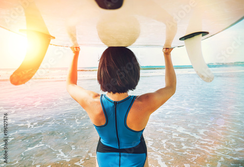 Woman takes surfboard on head and goes in ocean waves