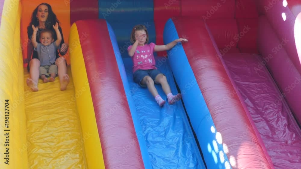 Slow motion family slides down a huge inflatable slide during a party