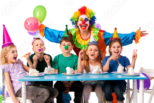 Birthday child clown playing with children who eat cake. Kid with nose bunny fingers prank. Fun of group people pose for camera sit at table white background. Mom arranged holiday for her daughter.