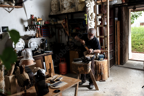 Senior man working on his wooden sculpture in his workshop.
