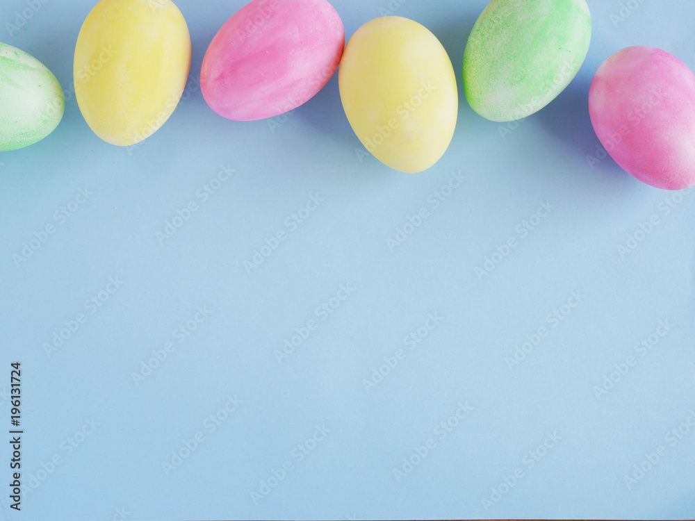 Painted Easter eggs in pastel colors (pink, yellow, green) on a paper blue background. Easter background, top view, flat layout.