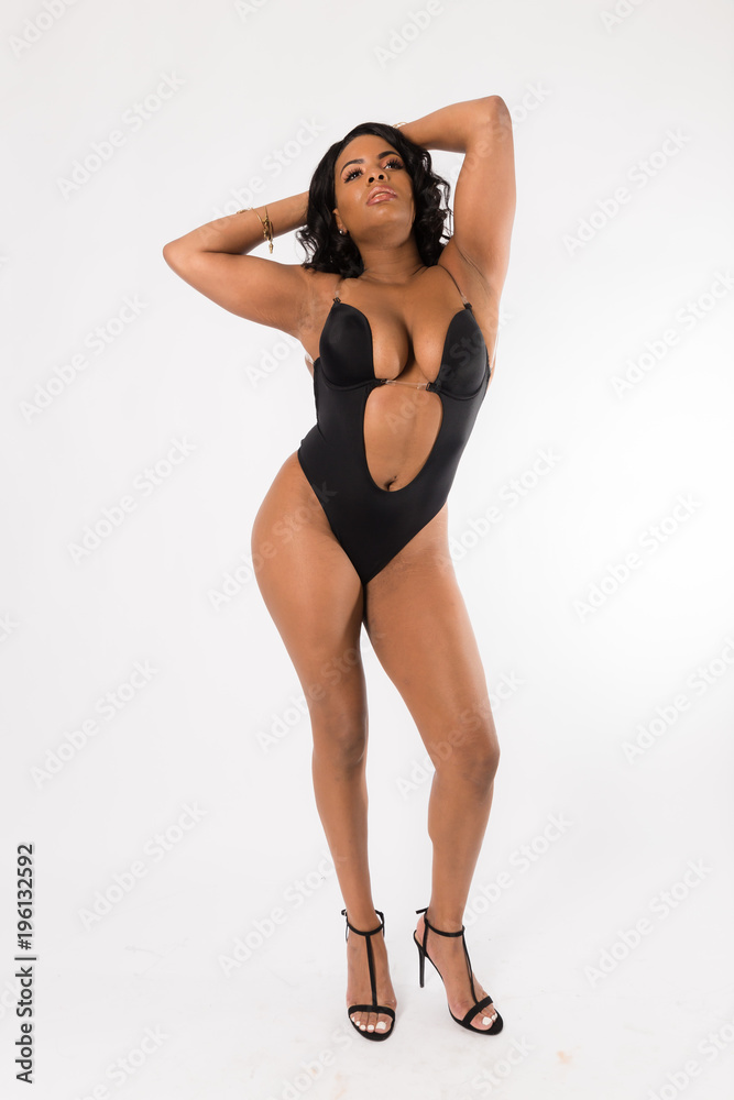 Fit young mixed race woman with long curly hair poses in a black two piece against a white background