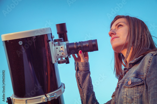 Cute young woman holding astronomical telescope and looking at the sky.