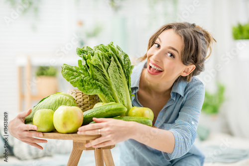 Portrait of a young and beautiful woman sitting with healthy green and fresh food indoors in the bright living room with green plants at home