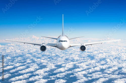 Passenger airplane flying at flight level high in the sky above the clouds and blue sky. View directly in front  exactly.