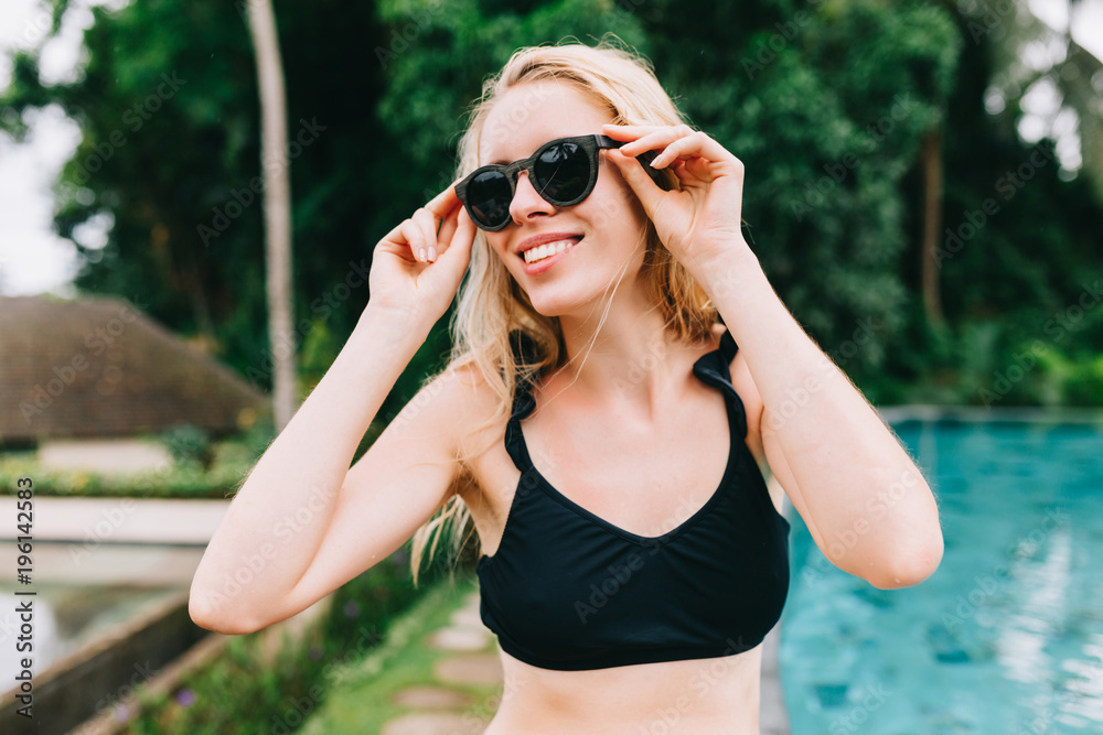 Portrait of happy cute young woman with fantastic smile enjoys the vacation on the background of the pool and jungles with great smile and happy true emotions Portrait of happy cute young woman with fantastic smile enjoys the vacation on the background of the pool and jungles with great smile and happy true emotions