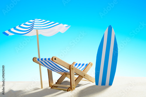 Fototapeta Naklejka Na Ścianę i Meble -  Deck chair under an umbrella and a surfboard on sandy beach